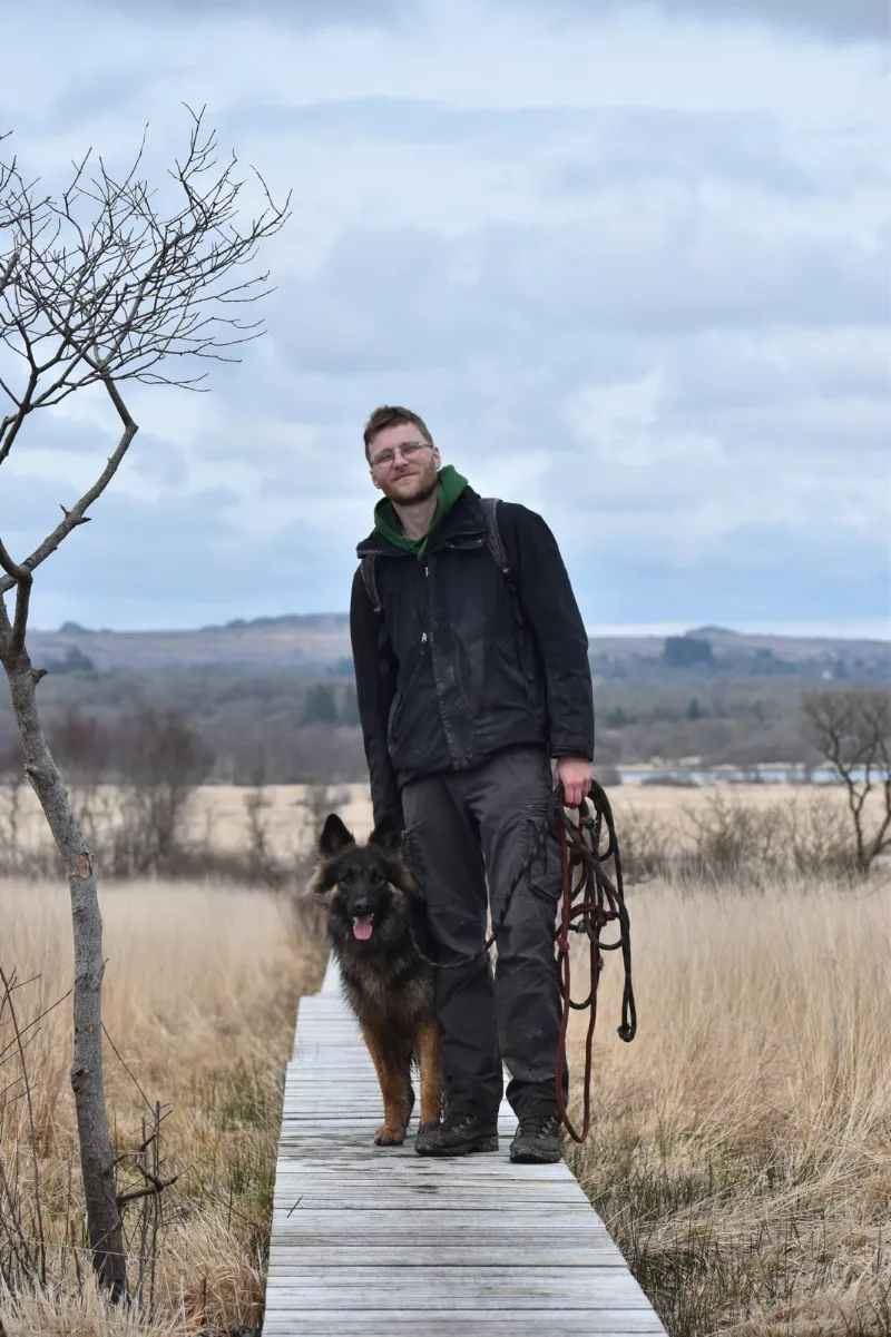 Jules marche sur un ponton de bois avec un chien, marais en arrière-plan