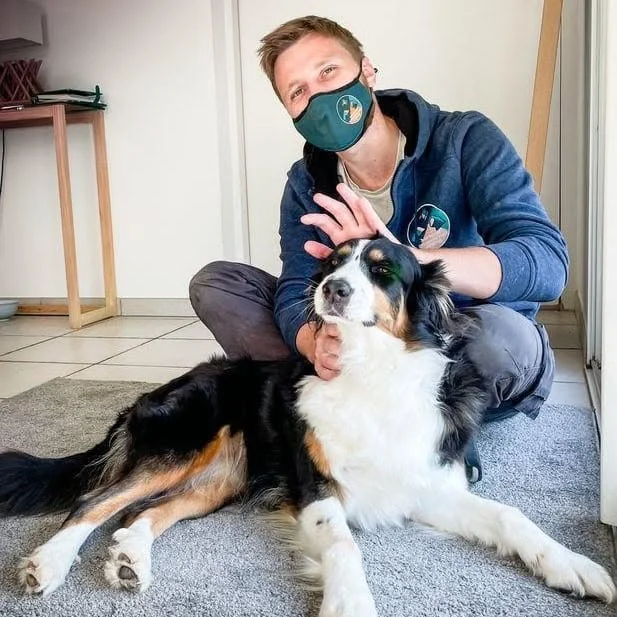 Jules regarde l’objectif, une main sur la tête d’un chien tricolore allongé sur le tapis
